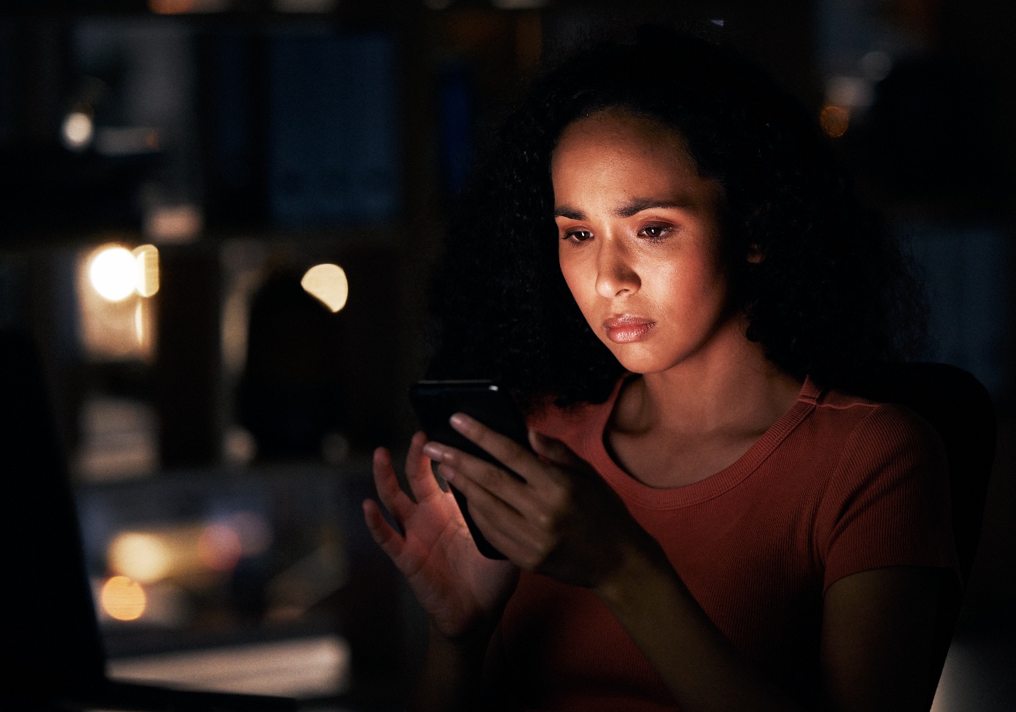A woman gazes at her phone illuminated by its light in a dark room